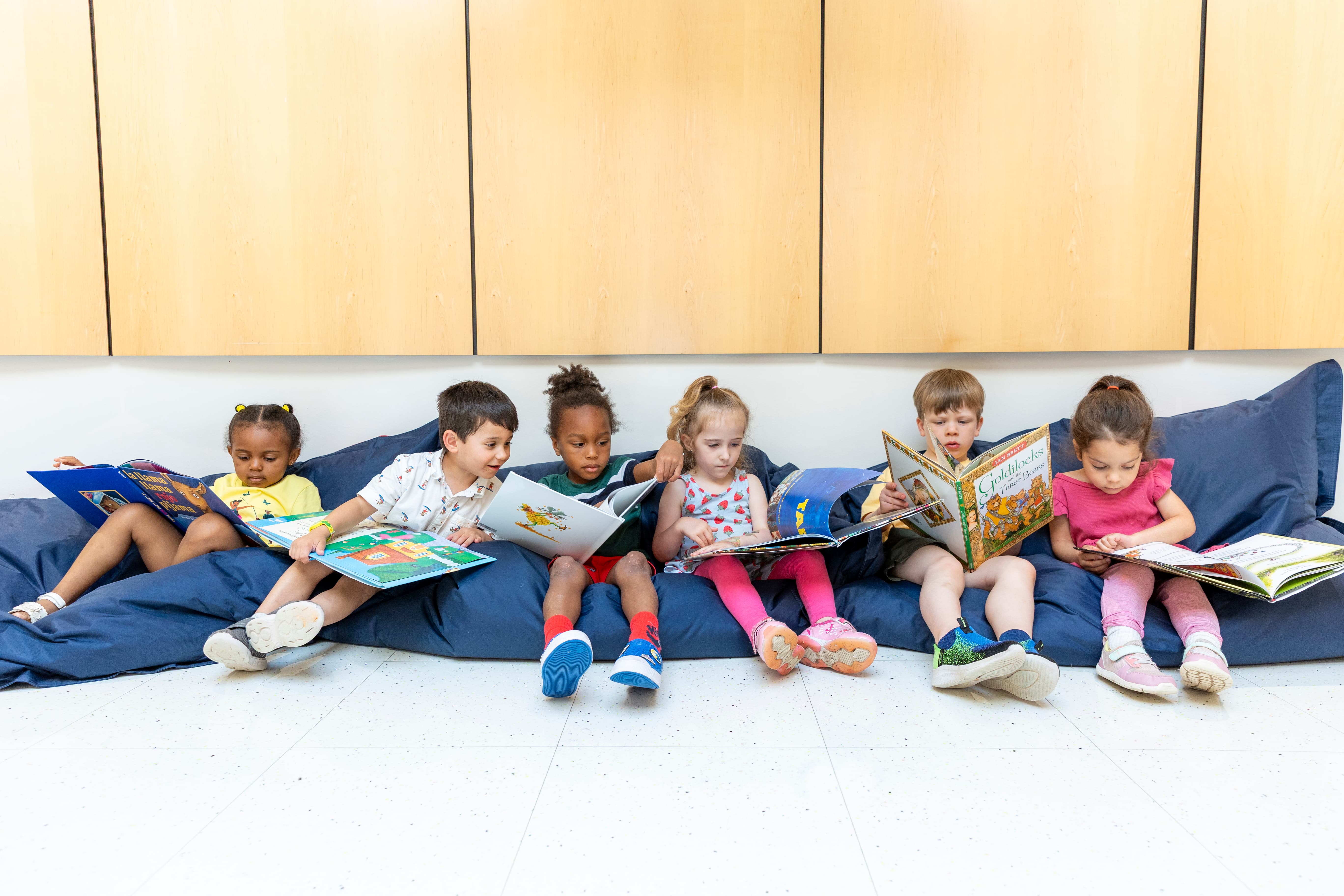 Young students at the New E3 School holding up books while reading