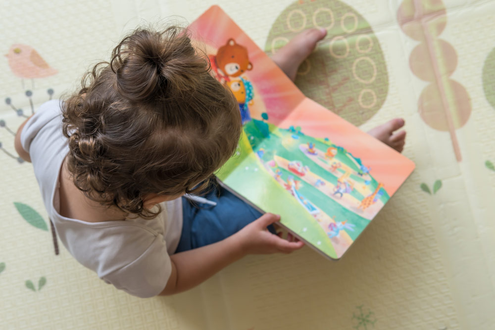 A young toddler reading a book on a play mat